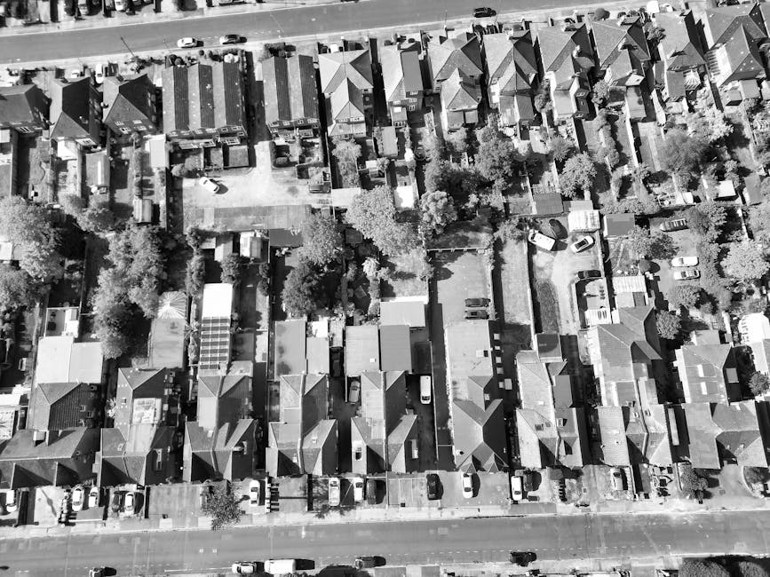 An aerial view of a residential garden area showing multiple small gardens and yards behind houses arranged in a row along a street. The gardens feature a variety of lawn patches, paved pathways, gard